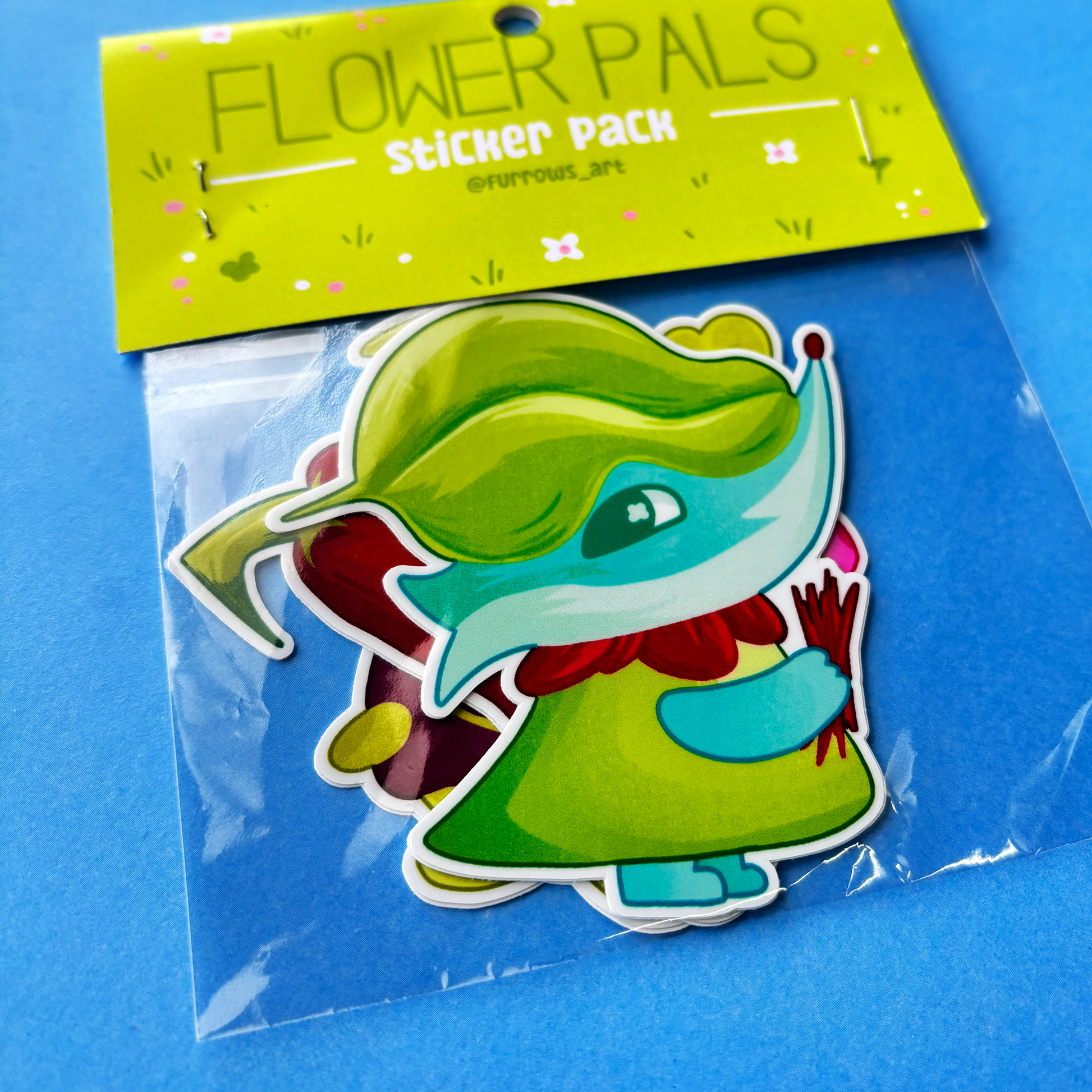 Sticker of a character with green hair and dress on a blue background with 'Flower Pals' sticker pack label.